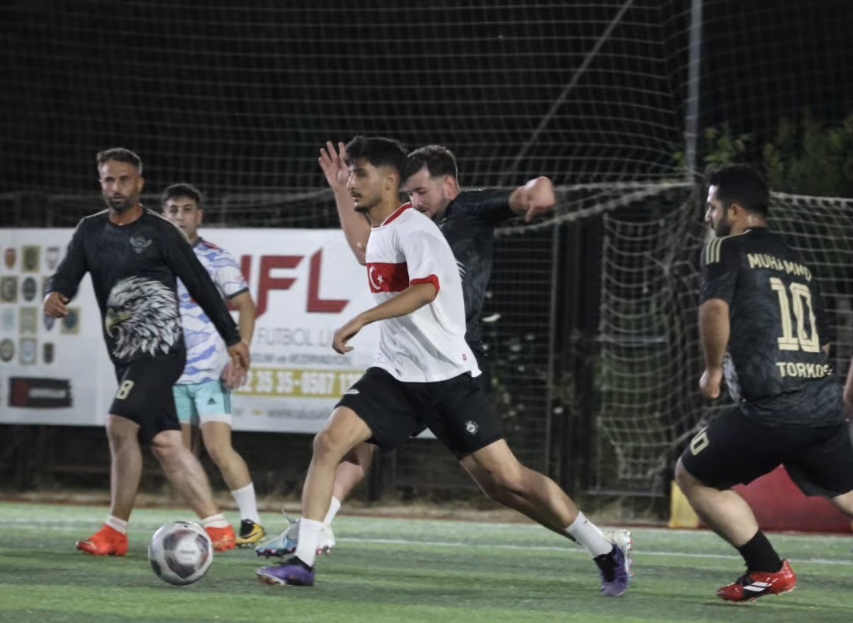 Ulusal Lig İzmir'de gece maçından bir top kapma anı — forma üzerinde ay-yıldız detayı olan oyuncu topla ilerliyor, arkada UFL Ulusal Futbol Ligi reklam panosu görünüyor